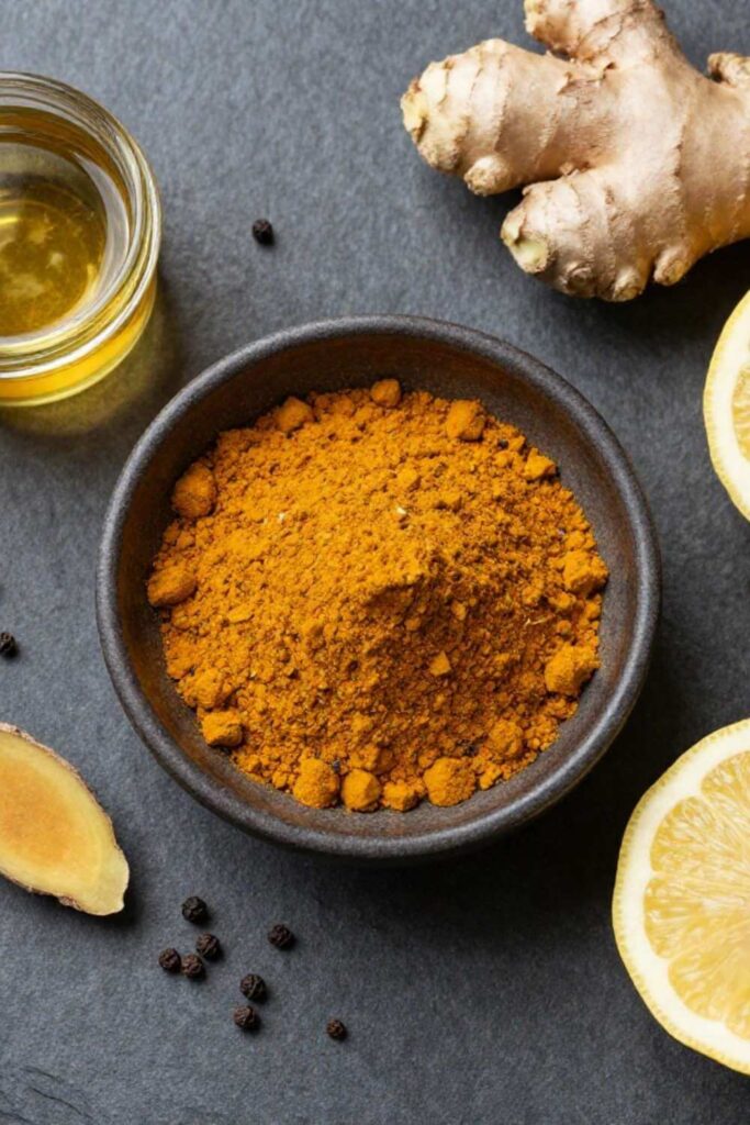 Ground turmeric in a ceramic bowl with black peppercorns and ginger on a stone surface, for a post about turmeric bioavailability and anti-inflammatory benefits on keto Mediterranean